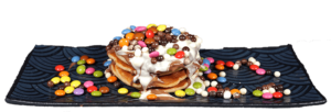 Pancakes mit Schokolade, weißer Schokolade und Smarties auf einem schwarzen Teller