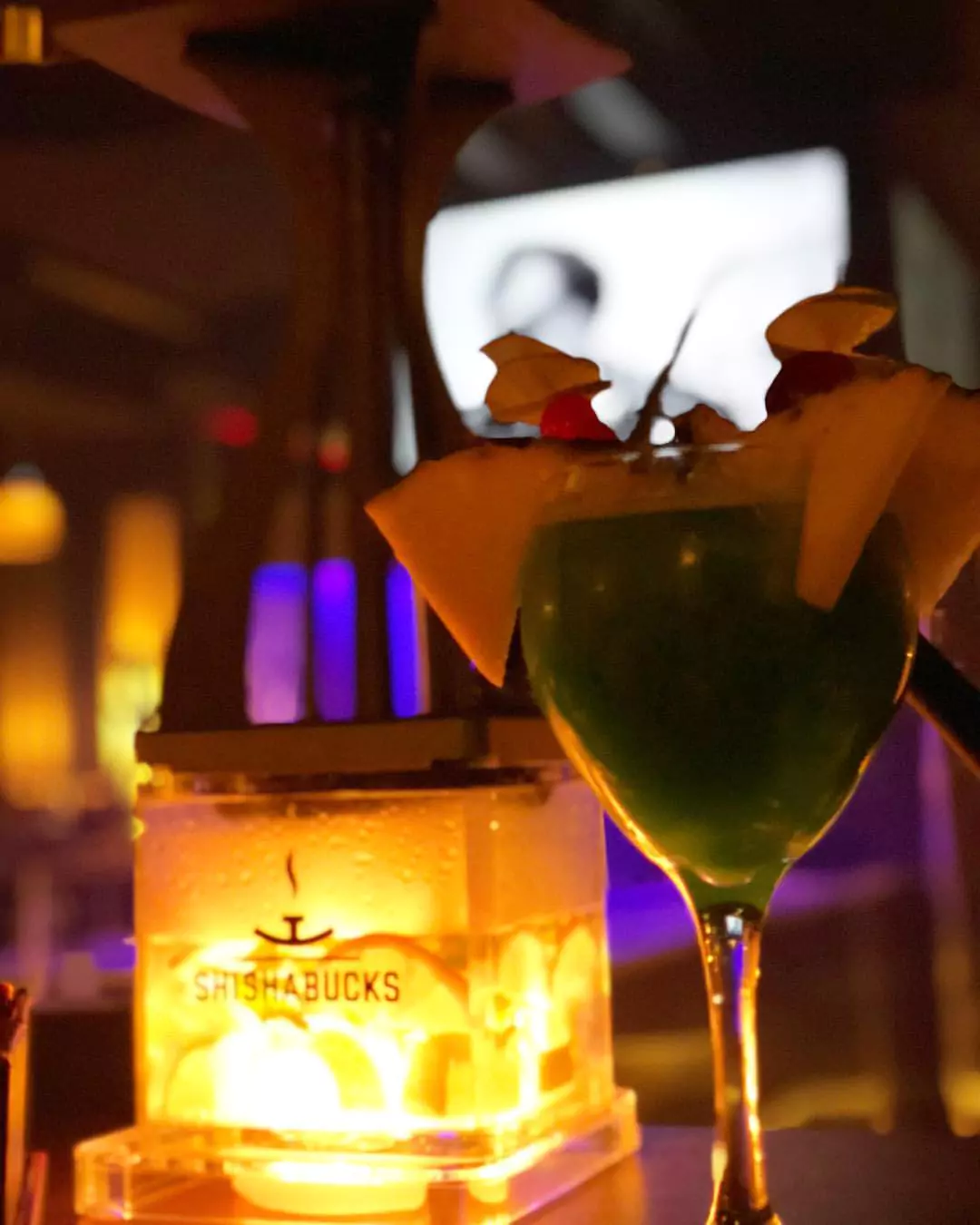 Ein erfrischender Cocktail neben einer beleuchteten Shisha in der stilvollen Shisha Bar Eimsbüttel, mit warmer und stimmungsvoller Beleuchtung.