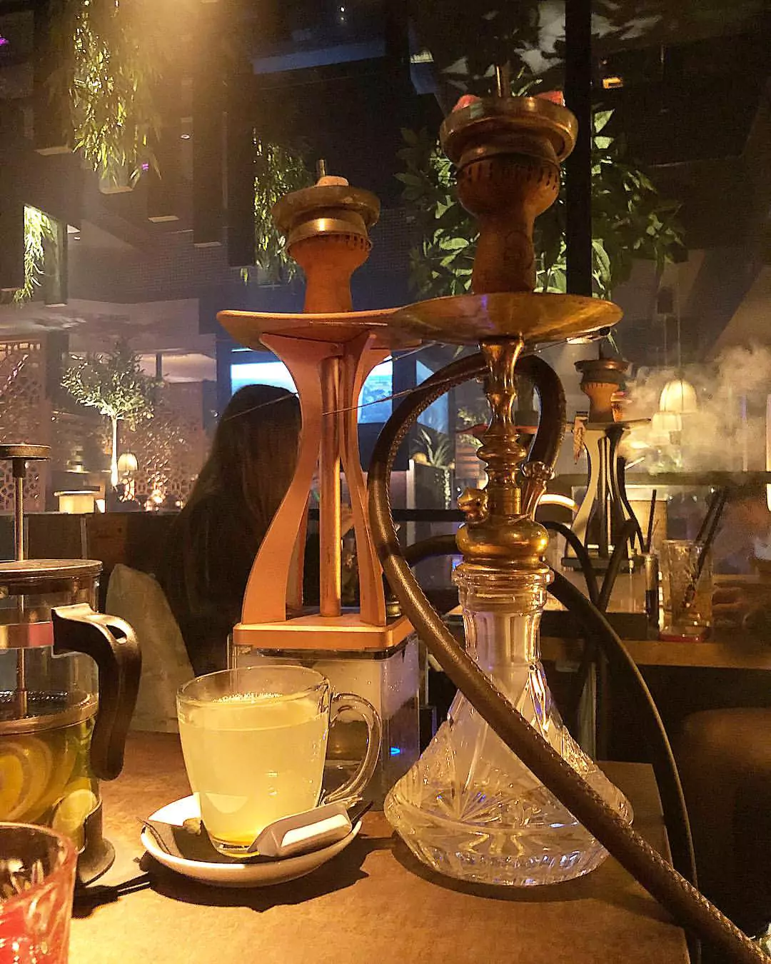 Eine Shisha und ein Glas Tee auf einem Tisch in der Shisha Bar Elbphilharmonie, umgeben von einer stilvollen und rauchigen Atmosphäre.