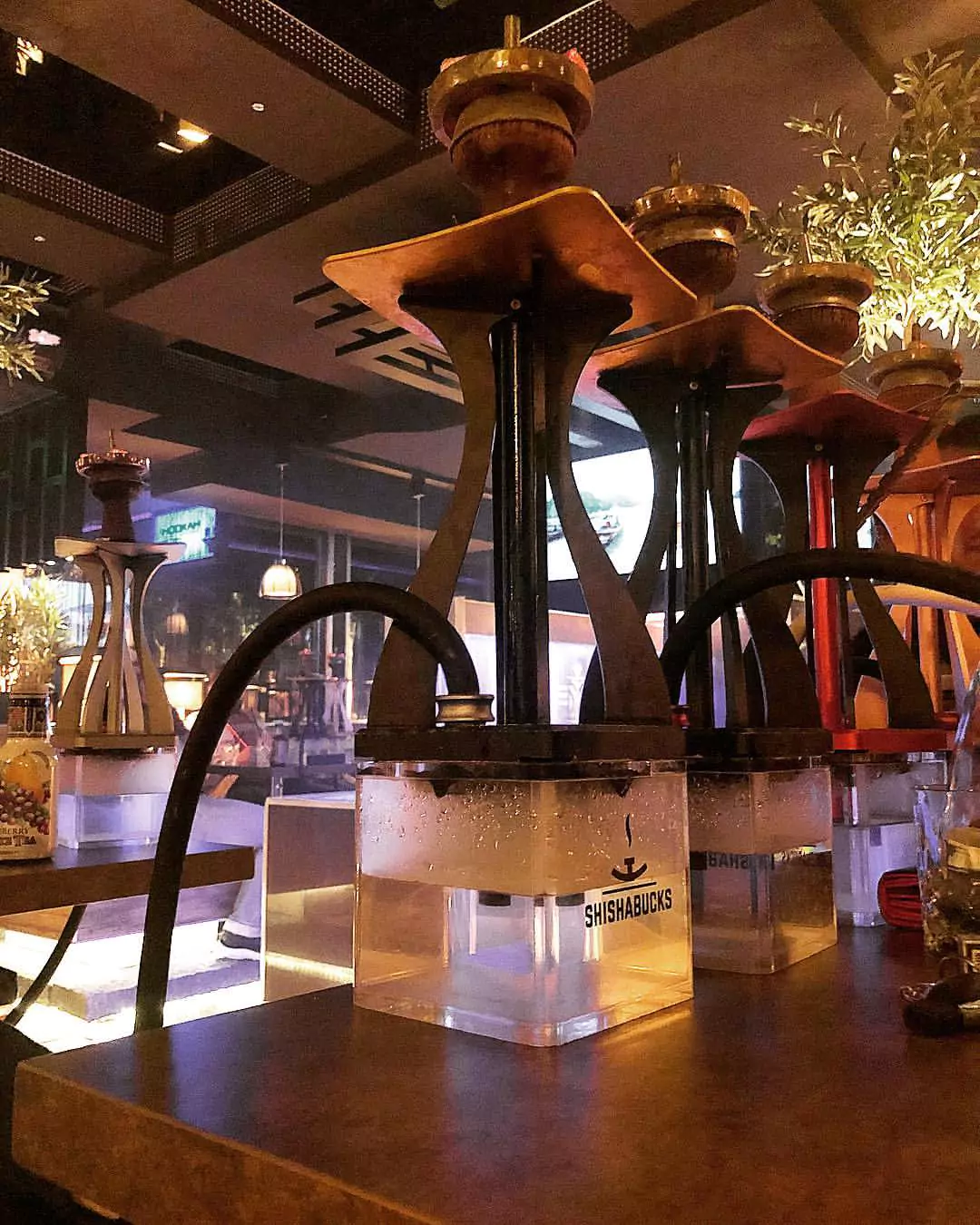 Moderne Shishas mit klaren Glas-Bowls in einer stilvollen Shisha-Bar, beleuchtet von warmem Umgebungslicht.