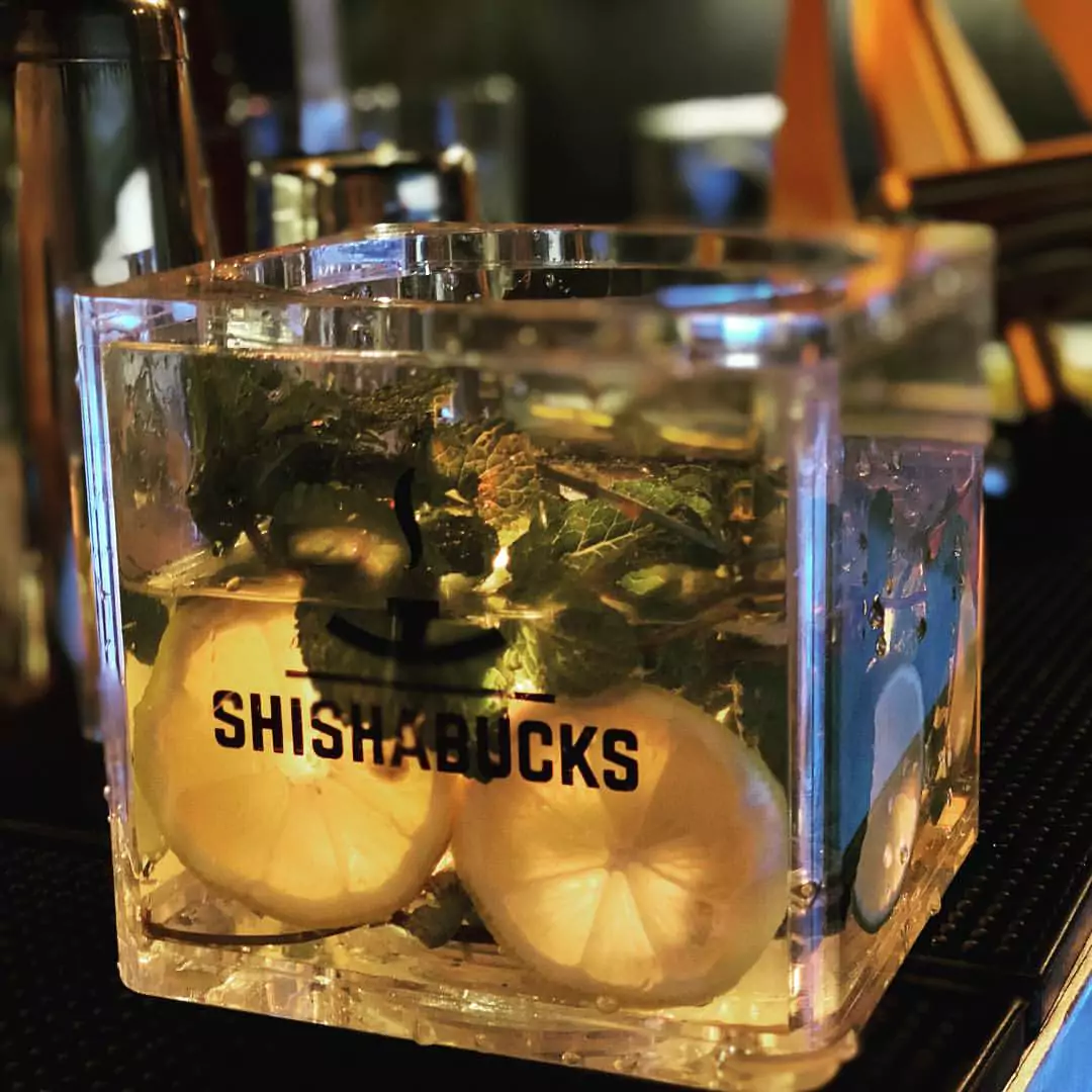 Eine Shishabucks Shisha in einer stilvollen Shisha Bar in Altona Hamburg, mit einer Glasbowl, gefüllt mit frischen Zitronenscheiben und Minzblättern.