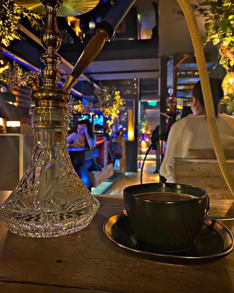 Eine luxuriöse Shisha neben einer Tasse Kaffee in der stilvollen Umgebung des Shisha Café Elbphilharmonie, mit entspannter Atmosphäre und stimmungsvoller Beleuchtung.