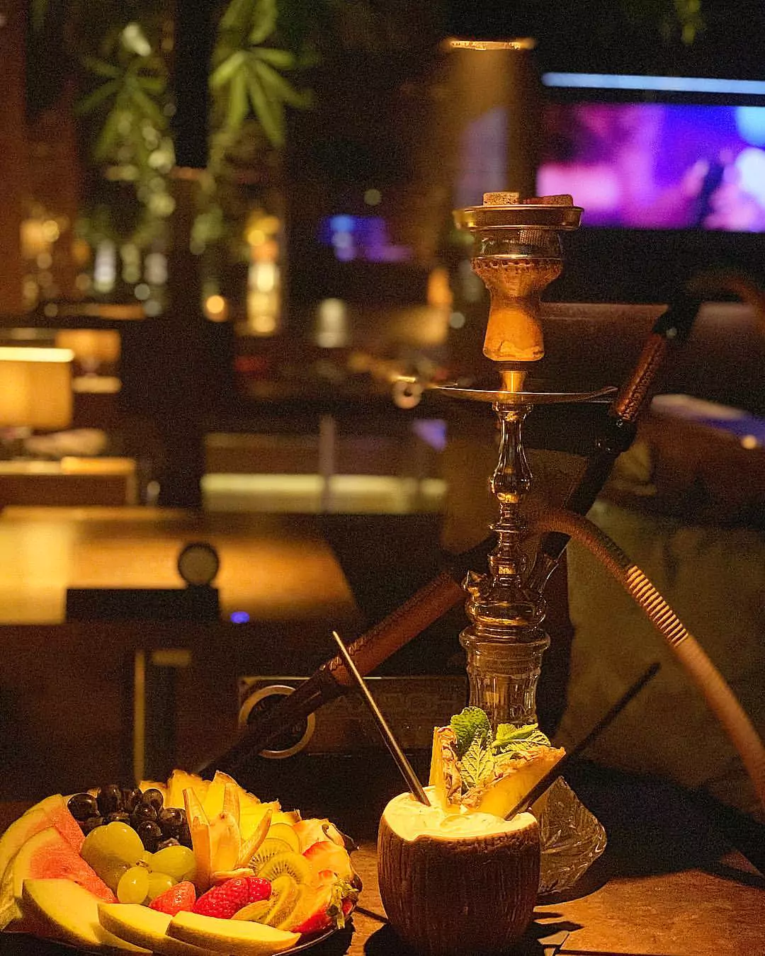 Shisha und frischer Obstteller in einem stilvollen Shisha-Café, beleuchtet von warmem Umgebungslicht.