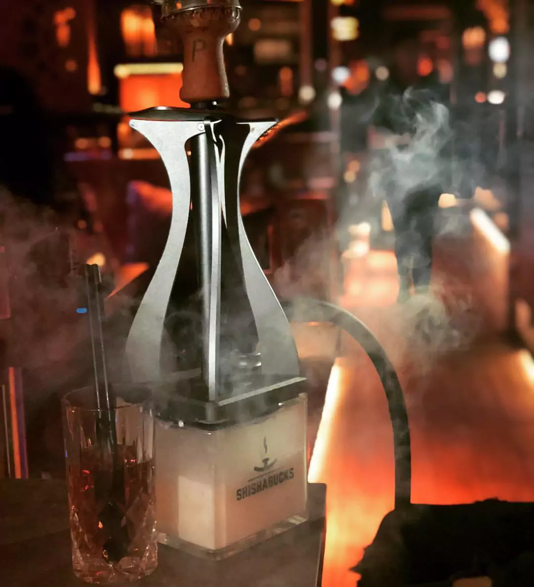 Eine moderne Shisha mit einem Getränk in einer stilvoll beleuchteten Umgebung in der Shisha Lounge Berliner Tor, umgeben von aufsteigendem Rauch.