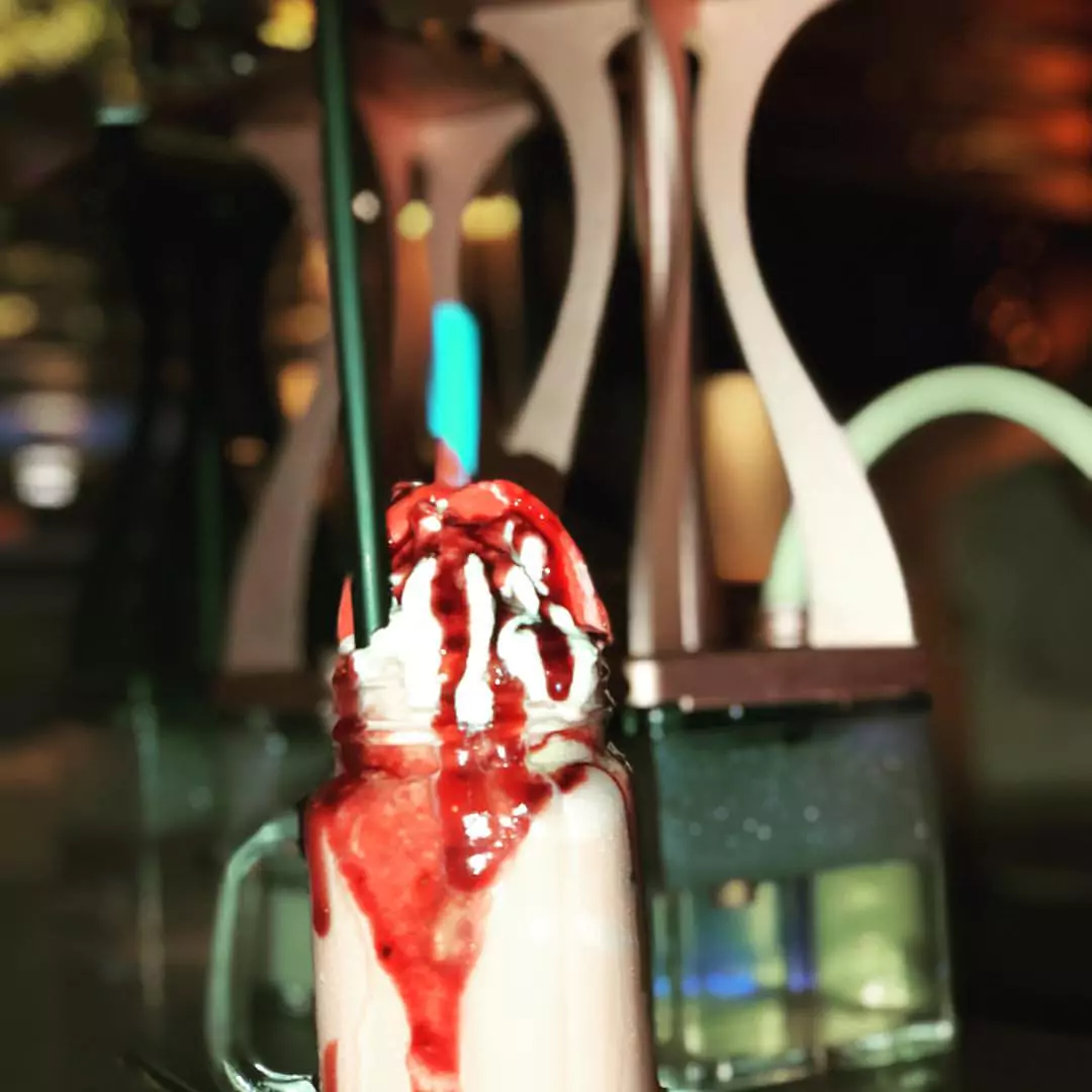 Ein kunstvoll dekorierter Milchshake mit Sahne und roter Soße, serviert neben einer modernen Shisha in einer Shisha Bar in Barmbek.