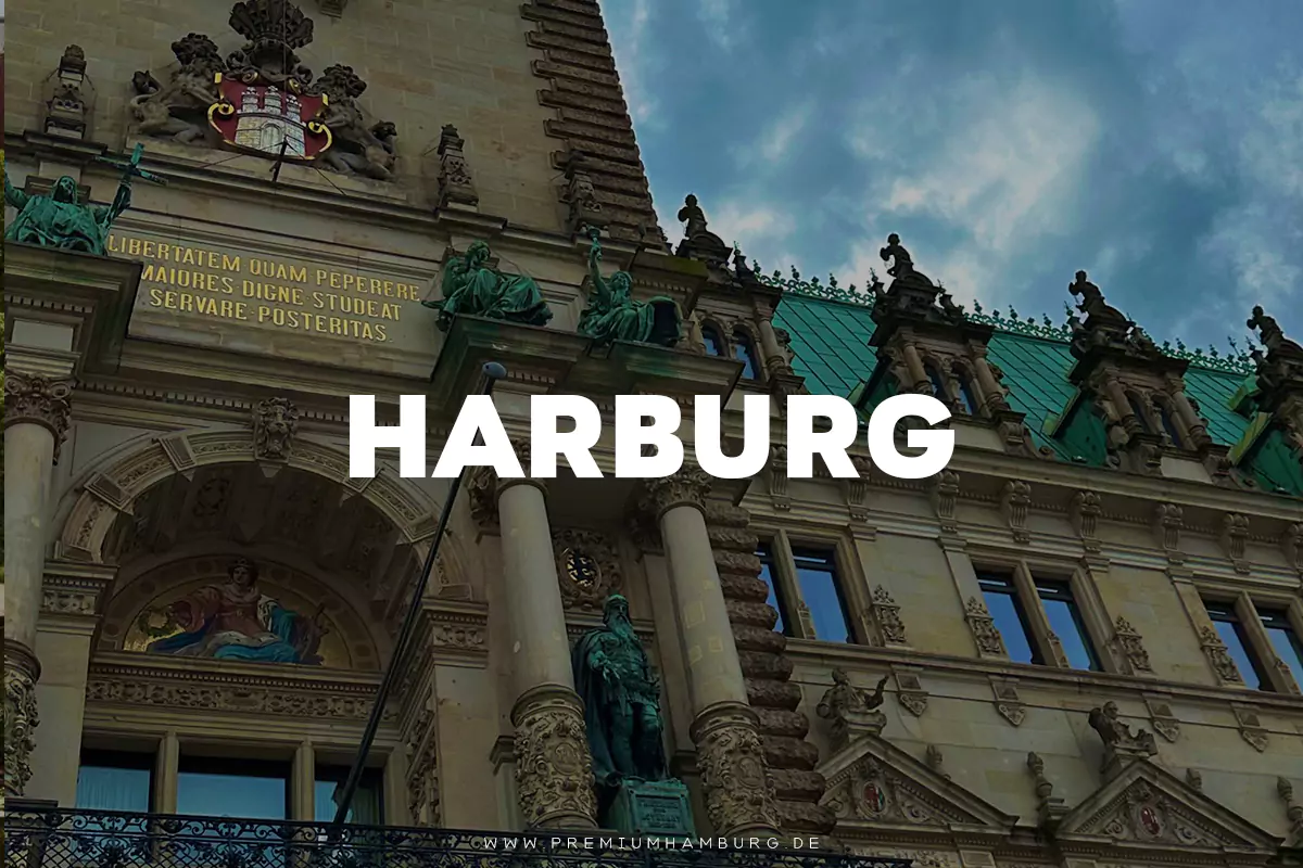 „Shisha Bar Hamburg Harburg“: Detailansicht eines historischen Gebäudes mit aufwendiger Fassade, verziert mit Statuen und einem Wappen, unter einem leicht bewölkten Himmel. Im Vordergrund ist der Schriftzug "HARBURG" prominent platziert.