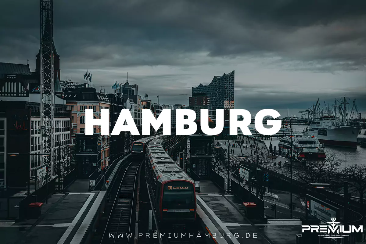 Blick auf eine U-Bahn in Hamburg, die vor der Kulisse der Elbphilharmonie und des Hafens fährt, mit dem großen Schriftzug „HAMBURG“. Shisha Hamburg